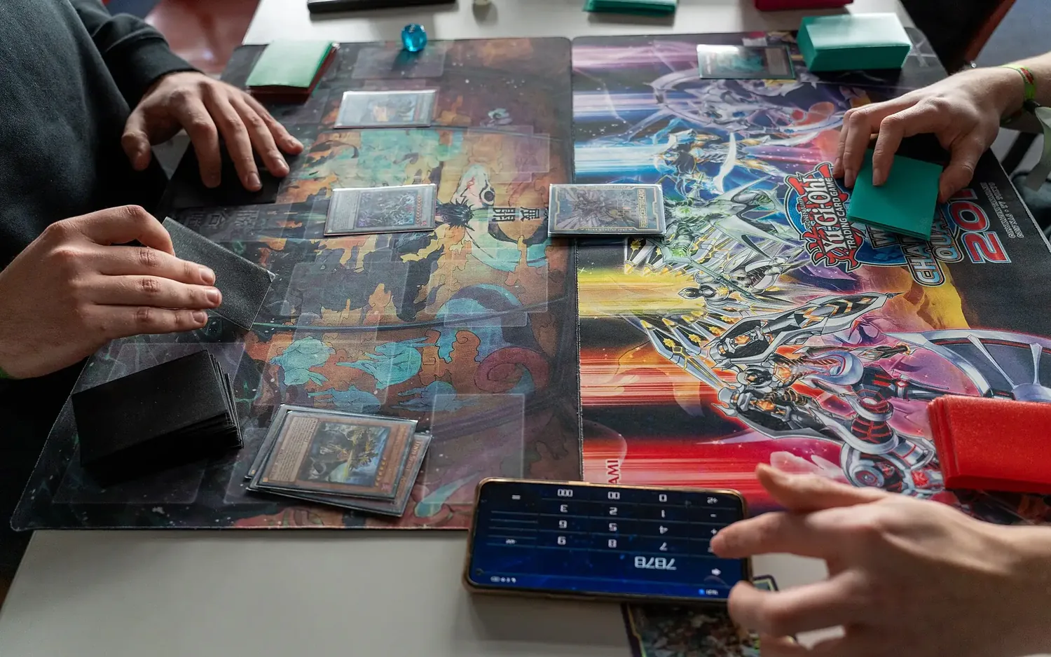 Two players mid-game with cards on playmats and a phone life counter
